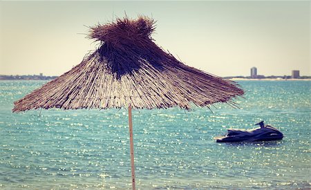 resort outdoor bed - Straw beach umbrella on a background of the cloudless sky and calm sea on a bright sunny day. Toned image. Shallow depth of field. Photographie de stock - Aubaine LD & Abonnement, Code: 400-08188417