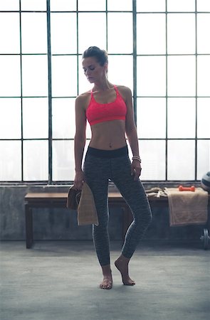 simsearch:400-08189778,k - Wearing comfortable workout gear, a woman is standing looking down at the ground in a loft gym, holding a towel. She is barefoot, getting ready to do a yoga workout. Foto de stock - Super Valor sin royalties y Suscripción, Código: 400-08189779