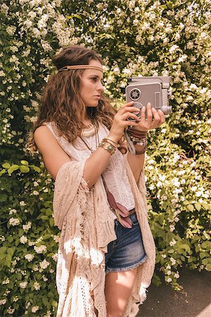 simsearch:400-08194027,k - Longhaired hippy-looking young lady in knitted shawl and white blouse standing among flowers with retro camera Photographie de stock - Aubaine LD & Abonnement, Code: 400-08194044