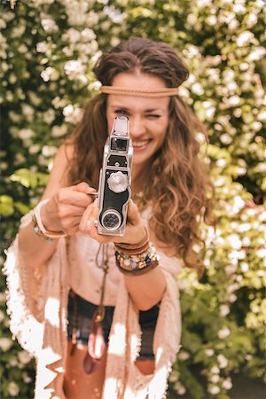 simsearch:400-08194027,k - Longhaired hippy-looking young lady in knitted shawl and white blouse standing among flowers with retro camera Photographie de stock - Aubaine LD & Abonnement, Code: 400-08194041