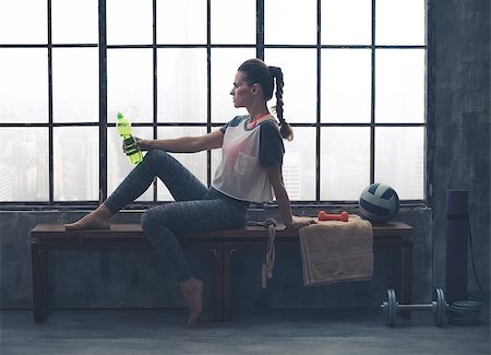 simsearch:400-08189778,k - An athletic woman wearing workout gear is sitting relaxing on a wooden bench in a loft gym. Having just finished her yoga workout, she is relaxing and holding a bottle of water. Foto de stock - Super Valor sin royalties y Suscripción, Código: 400-08195149