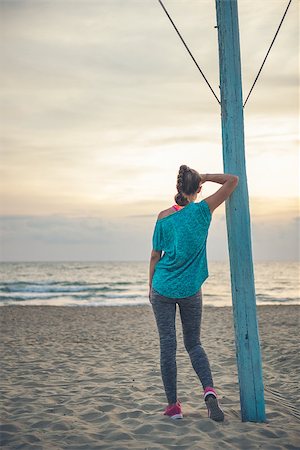 Leaning her arm against a flagpole, a fit woman is standing on the beach, admiring the sunset and the water. Stock Photo - Budget Royalty-Free & Subscription, Code: 400-08195191