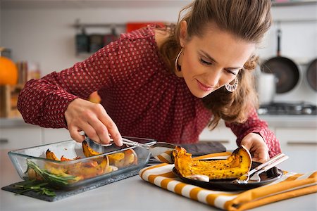 simsearch:400-07956018,k - An elegant woman in a kitchen focuses on serving a slice of roasted pumpkin onto a dark plate. Stockbilder - Microstock & Abonnement, Bildnummer: 400-08196820