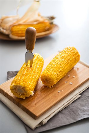 simsearch:400-04360453,k - Ready, set, eat... Two rich, yellow corncobs are sitting on a wooden board, ready to be eaten. In one, a corn cob skewer is planted, making it nice and easy to eat. Foto de stock - Royalty-Free Super Valor e Assinatura, Número: 400-08198048