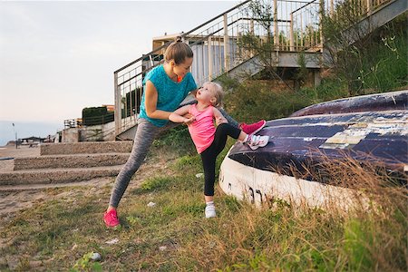 A mother in fitness gear is standing behind her daughter, guiding her in how to stretch out using an upturned boat. Happy and earnest, the little girl looks up at her mother lovingly. Stock Photo - Budget Royalty-Free & Subscription, Code: 400-08198092