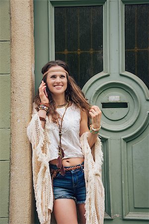 simsearch:400-08194027,k - Young trendy hipster woman standing outdoors against wooden door in old town and talking cell phone Photographie de stock - Aubaine LD & Abonnement, Code: 400-08198992