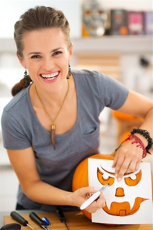 simsearch:400-07172678,k - Happy young woman in kitchen using stencils to carve scary pumpkin Jack-O-Lantern for Halloween party Photographie de stock - Aubaine LD & Abonnement, Code: 400-08199665