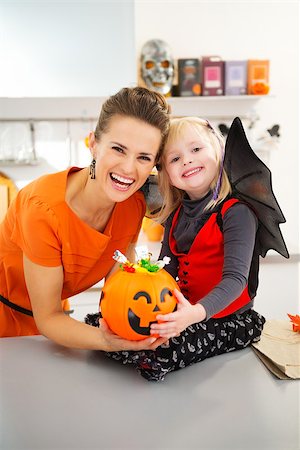 Portrait of halloween dressed girl with happy mother holding big pumpkin bucket full of candy in decorated kitchen.  Halloween Candy is so good. Traditional autumn holiday Stock Photo - Budget Royalty-Free & Subscription, Code: 400-08199929