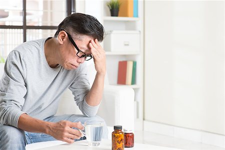 simsearch:400-05251905,k - Portrait of 50s mature Asian man headache, massaging head with painful expression, sitting on sofa at home, medicines and water on table. Stock Photo - Budget Royalty-Free & Subscription, Code: 400-08225180