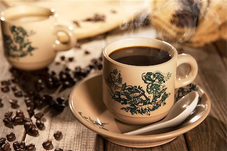 Steaming traditional Chinese nan yang style coffee in vintage mug and saucer with coffee beans. Fractal on the cup is generic print. Soft focus setting with dramatic ambient light on dark wooden background. Foto de stock - Royalty-Free Super Valor e Assinatura, Número: 400-08223385