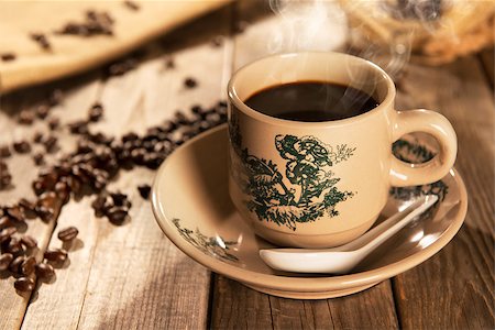 Steaming traditional Chinese style coffee in vintage mug and saucer with coffee beans. Fractal on the cup is generic print. Soft focus setting with dramatic ambient light on dark wooden background. Foto de stock - Royalty-Free Super Valor e Assinatura, Número: 400-08223383