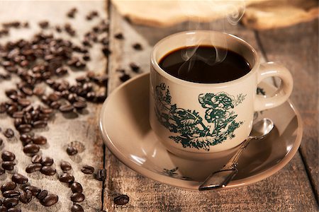 Steaming traditional Chinese Hainan style coffee in vintage mug and saucer with coffee beans. Fractal on the cup is generic print. Soft focus setting with dramatic ambient light on dark wooden background. Foto de stock - Royalty-Free Super Valor e Assinatura, Número: 400-08223397