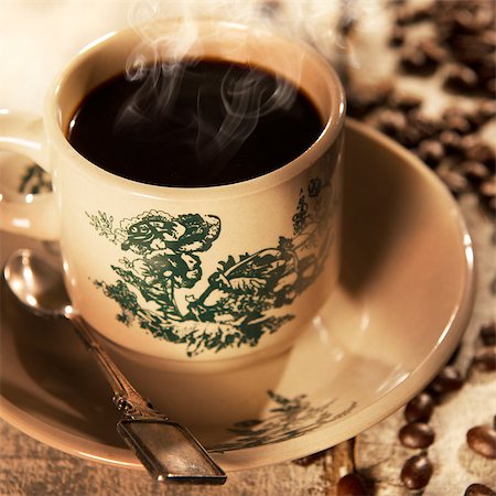 Steaming traditional Hainanese style black coffee in vintage mug and saucer with coffee beans. Fractal on the cup is generic print. Soft focus setting with dramatic ambient light on dark wooden background. Foto de stock - Royalty-Free Super Valor e Assinatura, Número: 400-08223398