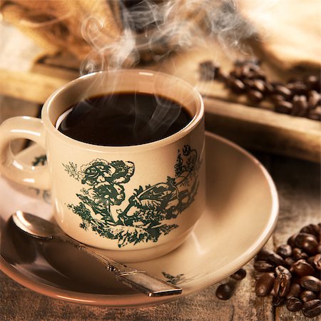 Steaming traditional Hainan style dark coffee in vintage mug and saucer with coffee beans. Fractal on the cup is generic print. Soft focus setting with dramatic ambient light on dark wooden background. Foto de stock - Royalty-Free Super Valor e Assinatura, Número: 400-08223399