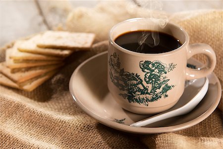 Steaming traditional oriental Chinese kopitiam style dark coffee in vintage mug and saucer with soda crackers. Fractal on the cup is generic print. Soft focus setting with dramatic ambient light on dark wooden background. Foto de stock - Royalty-Free Super Valor e Assinatura, Número: 400-08223405