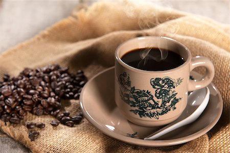 Steaming traditional oriental Chinese kopitiam style dark coffee in vintage mug and saucer with coffee beans. Fractal on the cup is generic print. Soft focus setting with dramatic ambient light on dark wooden background. Foto de stock - Royalty-Free Super Valor e Assinatura, Número: 400-08223407