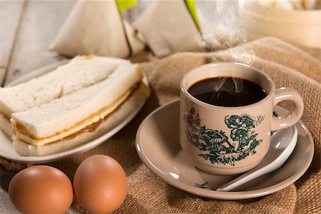 Traditional kopitiam style Malaysian coffee in vintage mug and saucer and breakfast. Fractal on the cup is generic print. Soft focus dramatic ambient light over wood table. Foto de stock - Royalty-Free Super Valor e Assinatura, Número: 400-08223409