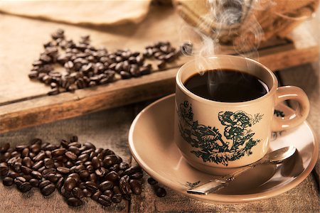 Steaming traditional Chinese style dark coffee in vintage mug and saucer with coffee beans. Fractal on the cup is generic print. Soft focus setting with dramatic ambient light on dark wooden background. Foto de stock - Royalty-Free Super Valor e Assinatura, Número: 400-08223400