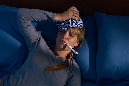 simsearch:695-05764382,k - Young hispanic woman in pajamas, laying on bed with fever and ice bag on head, measuring temperature with digital thermometer at night. High angle view Stock Photo - Budget Royalty-Free & Subscription, Code: 400-08223659