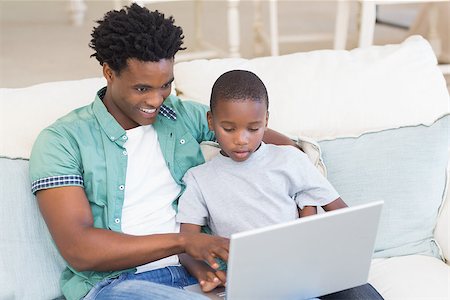 Father and son using laptop on the couch at home in the living room Stock Photo - Budget Royalty-Free & Subscription, Code: 400-08265499