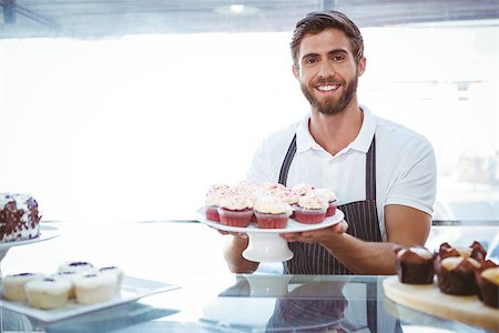 simsearch:400-08265905,k - Smiling worker holding cupcakes behind the counter at bakery Foto de stock - Super Valor sin royalties y Suscripción, Código: 400-08265928