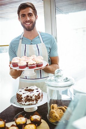 simsearch:400-08265905,k - Smiling worker holding cupcakes behind the counter at bakery Foto de stock - Super Valor sin royalties y Suscripción, Código: 400-08265935