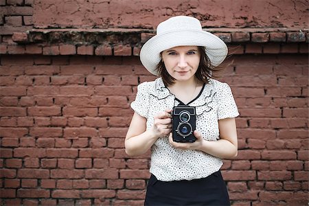 simsearch:400-07464688,k - Woman photographer in white hat with old retro camera on a background old vintage brown brick wall. Selective focus on model. Natural light. Vintage style photo. Photographie de stock - Aubaine LD & Abonnement, Code: 400-08284319