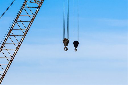 Two dirty industrial crane hoist hooks and pulleys hanging by steel cables with crane truss on left, against blue and white sky. Fotografie stock - Microstock e Abbonamento, Codice: 400-08285592