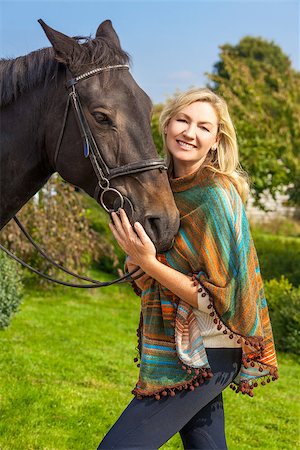 simsearch:400-08299085,k - Beautiful happy woman wearing poncho, smiling and leading her horse in sunshine Stock Photo - Budget Royalty-Free & Subscription, Code: 400-08294701