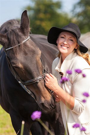 simsearch:400-08299085,k - Beautiful happy middle aged woman wearing black floppy hat, smiling and stroking her horse in sunshine Stock Photo - Budget Royalty-Free & Subscription, Code: 400-08299085