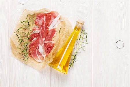 smoked ham - Prosciutto with rosemary and olive oil on wooden table. Top view with copy space Foto de stock - Super Valor sin royalties y Suscripción, Código: 400-08291217