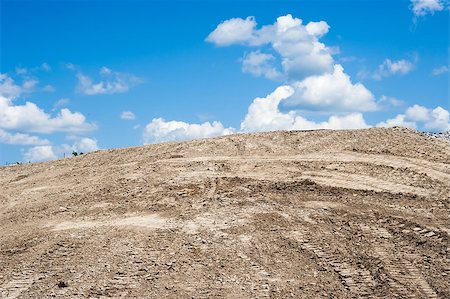 Sandy dirt mound with tire and caterpillar tracks, ending at blue sky with cumulus clouds. Fotografie stock - Microstock e Abbonamento, Codice: 400-08303802