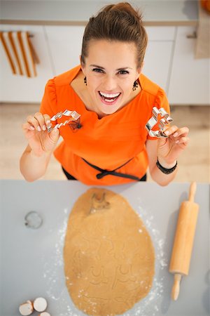 simsearch:400-08336563,k - Cheerful young woman holding cookie cutters for Halloween biscuits in kitchen. Traditional autumn holiday. Upper view Foto de stock - Royalty-Free Super Valor e Assinatura, Número: 400-08336560