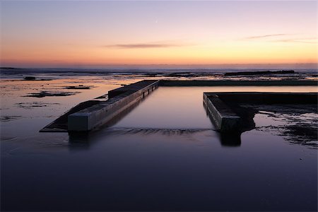 Dawn skies colour the reflections in he water covered rockshelf and the overflow from the pool and the tiniest sliver of a moon in the sky avove. Fotografie stock - Microstock e Abbonamento, Codice: 400-08337375