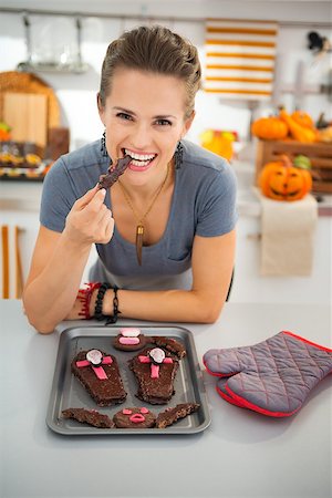 simsearch:400-08336563,k - Happy modern housewife in decorated kitchen eating freshly homemade Halloween biscuits for Trick or Treat. Traditional autumn holiday Foto de stock - Royalty-Free Super Valor e Assinatura, Número: 400-08337743