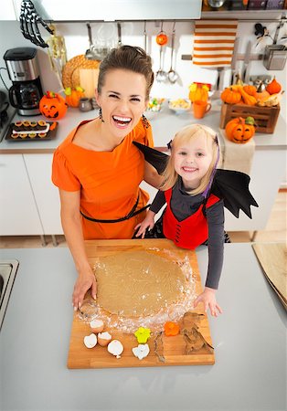 simsearch:400-08336563,k - Happy young mother with daughter in bat costume cutting out Halloween cookies with pastry cutter from rolled pastry in decorated kitchen. Traditional autumn holiday Foto de stock - Royalty-Free Super Valor e Assinatura, Número: 400-08337760