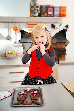 simsearch:400-08336563,k - Blond girl in bat costume in decorated kitchen eating freshly homemade Halloween biscuits for Trick or Treat. Ready to halloween party. Traditional autumn holiday Foto de stock - Royalty-Free Super Valor e Assinatura, Número: 400-08337774