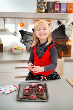 simsearch:400-08336563,k - Funny blond girl in bat costume in decorated kitchen holding freshly baked Halloween cookies for Trick or Treat. Ready to halloween party. Traditional autumn holiday Foto de stock - Royalty-Free Super Valor e Assinatura, Número: 400-08337773