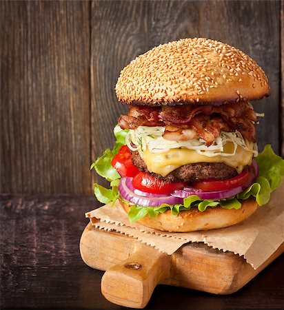 Big delicious cheeseburger stacked high with a bacon, beef patty, coleslaw, cheese, lettuce, red onion and tomato on sesame seed bun served on wooden cutting board. Stock Photo - Budget Royalty-Free & Subscription, Code: 400-08338455