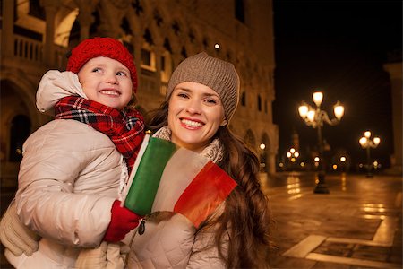 simsearch:400-08344334,k - Holiday family trip to Venice, Italy can change the whole Christmas experience. Happy mother and child holding Italian flag standing on Piazza San Marco in the evening. Winter Tourism Stock Photo - Budget Royalty-Free & Subscription, Code: 400-08344333
