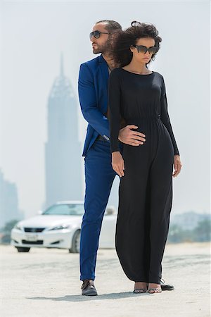 dubai men dress - Stylish couple arrived in a white car to walk on a deserted beach in Dubai on the background of skyscrapers. The dark-haired girl in a black dress and sunglasses. The dark-haired man with a beard wearing a blue suit hugging his girlfriend.  UAE. Vertical photo Stock Photo - Budget Royalty-Free & Subscription, Code: 400-08346848