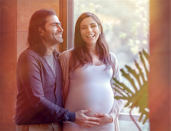 Portrait of handsome man touching tummy of his pregnant wife, standing near window in bright sunlight, happy pregnancy time Stock Photo - Royalty-Free, Artist: Anna_Omelchenko, Image code: 400-08348154
