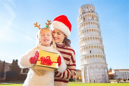 simsearch:400-08341864,k - Happy mother in Christmas hat hugging daughter wearing funny reindeer antlers and holding gift box in front of Leaning Tour of Pisa, Italy. They spending exciting Christmas time traveling. Fotografie stock - Microstock e Abbonamento, Codice: 400-08340909