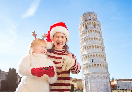 simsearch:400-08341864,k - Happy mother in Christmas hat pointing in camera and daughter in funny reindeer antlers holding photo camera. Leaning Tour of Pisa, Italy in background. Exciting Christmas time travel. Fotografie stock - Microstock e Abbonamento, Codice: 400-08340915