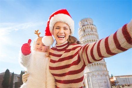 simsearch:400-08341864,k - Happy mother in Christmas hat taking selfie with daughter wearing funny reindeer antlers and showing thumbs up in front of Leaning Tour of Pisa, Italy. They spending exciting Christmas time traveling Fotografie stock - Microstock e Abbonamento, Codice: 400-08340919