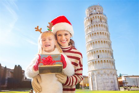 simsearch:400-08341864,k - Portrait of happy mother in Christmas hat hugging daughter wearing funny reindeer antlers and holding gift box in front of Leaning Tour of Pisa, Italy. They spending exciting Christmas time traveling. Fotografie stock - Microstock e Abbonamento, Codice: 400-08340910