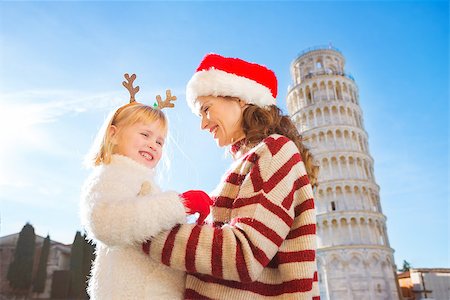 simsearch:400-08341864,k - Smiling mother in Christmas hat and cosy sweater and daughter wearing funny reindeer antlers standing in front of Leaning Tour of Pisa, Italy. They spending exciting Christmas time traveling. Fotografie stock - Microstock e Abbonamento, Codice: 400-08340922