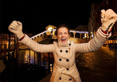 Happy elegant young woman in white coat rejoicing while standing in front of Rialto Bridge in the evening. She having Christmas time trip and enjoying stunning views of Venice, Italy Stock Photo - Budget Royalty-Free & Subscription, Code: 400-08341862