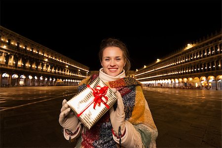 simsearch:400-08344334,k - Excitement of Christmas time and allure of long-time favourite Venice, Italy. Portrait of smiling woman holding Christmas gift box while standing on Piazza San Marco in the evening Stock Photo - Budget Royalty-Free & Subscription, Code: 400-08343467