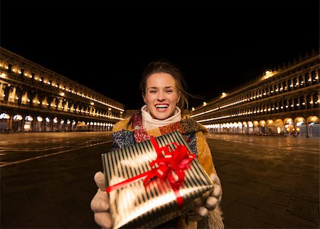 simsearch:400-08344334,k - Excitement of Christmas time and allure of long-time favourite Venice, Italy. Happy woman showing Christmas gift box while standing on Piazza San Marco in the evening Stock Photo - Budget Royalty-Free & Subscription, Code: 400-08343471